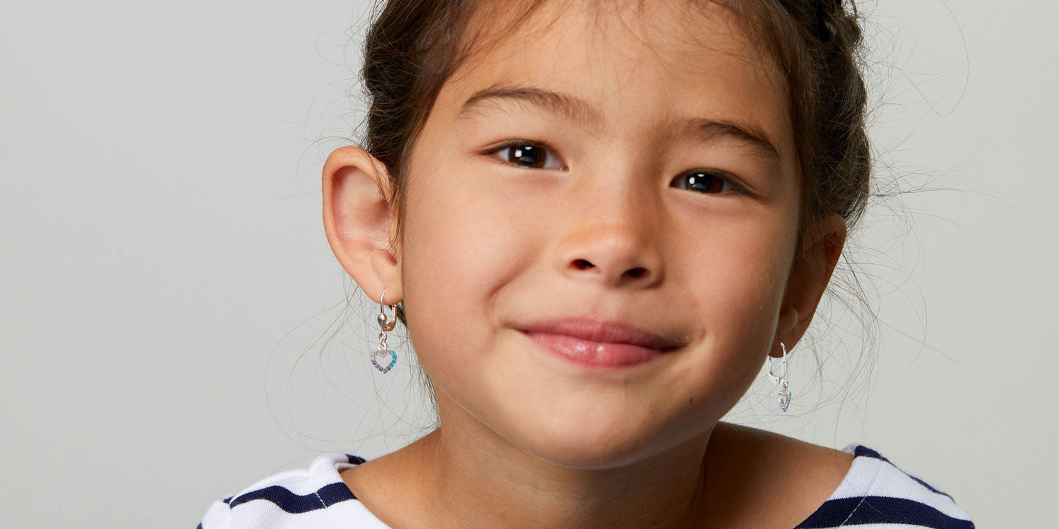 Lächelndes Mädchen mit dunklen Haaren in gestreiftem Shirt trägt bunte hängende Ohrringe mit Herz-Anhängern 