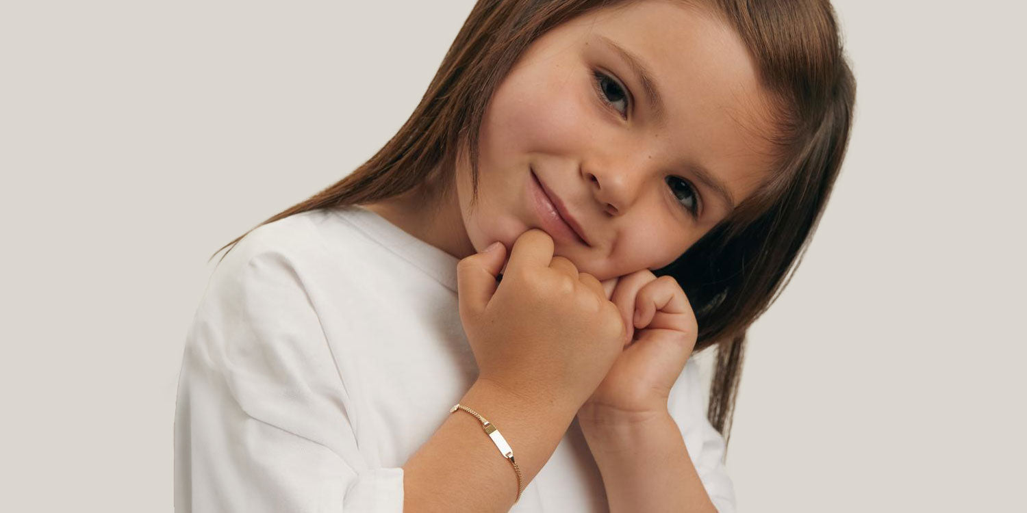 Süßes Mädchen mit braunen Haaren in weißem Langarmshirt trägt goldenes Armband und lächelt schüchtern