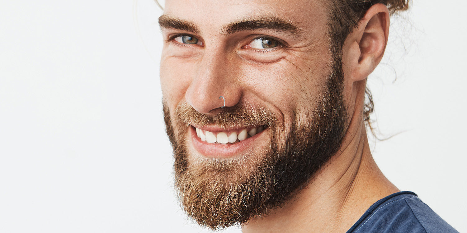 Lächelnder Mann mit Bart trägt einen kleinen Nasenring, Nahaufnahme-Portrait zeigt Gesichtsschmuck