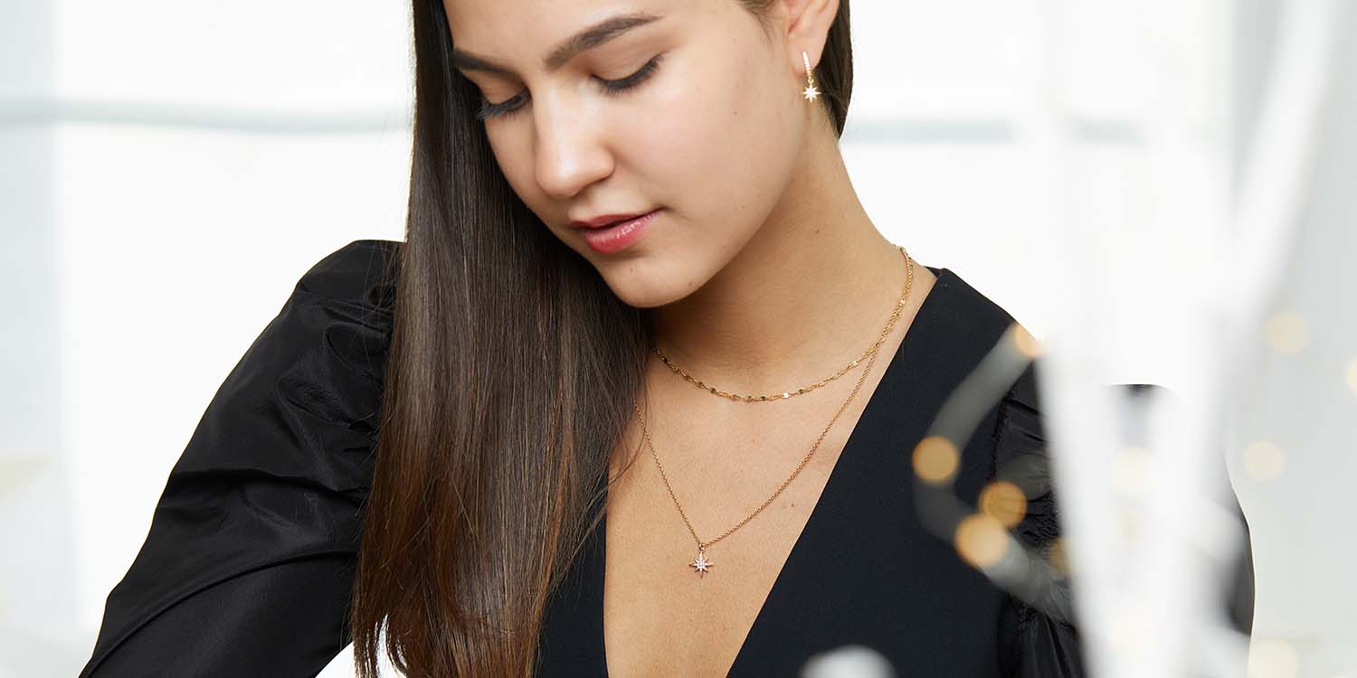 Frau in schwarzem Blazer trägt goldene Layering-Halsketten und Stern-Ohrringe