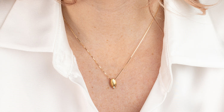 Goldene Halskette mit tropfenförmigem Anhänger am Dekolleté getragen