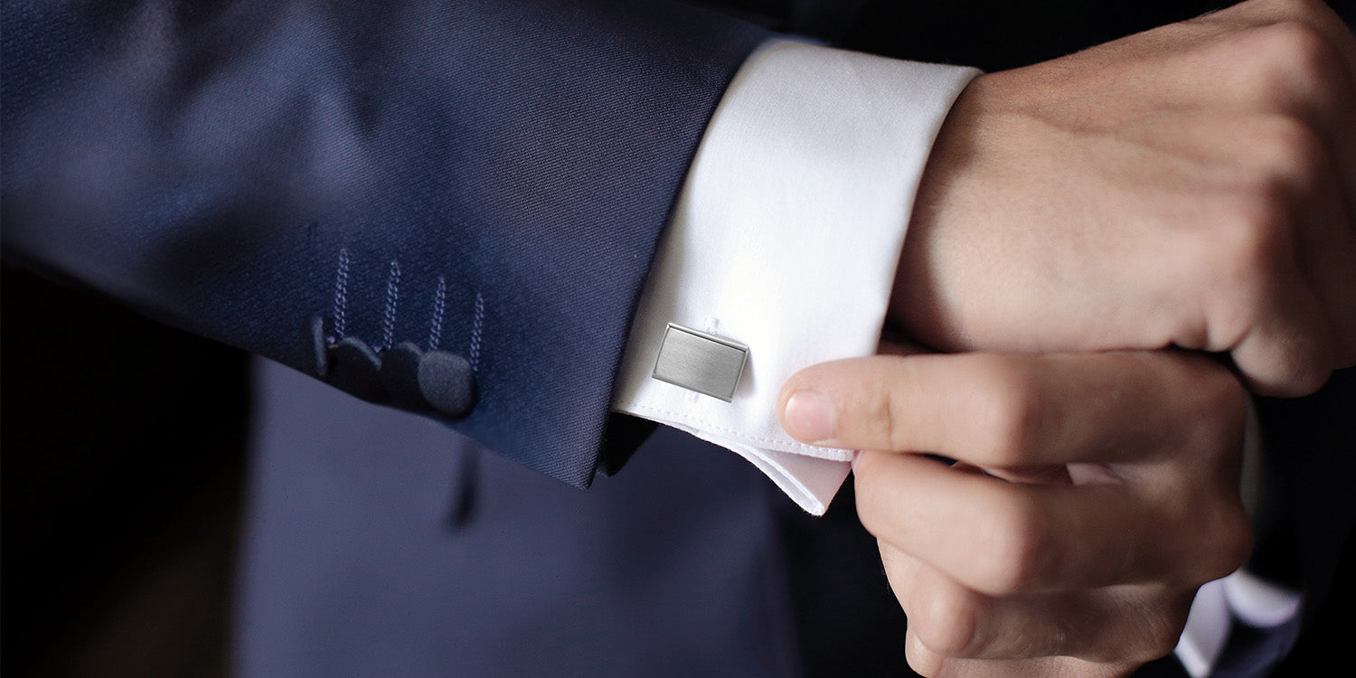 Eleganter Mann in dunkelblauem Anzug richtet silberne rechteckige Manschettenknöpfe am weißen Hemd