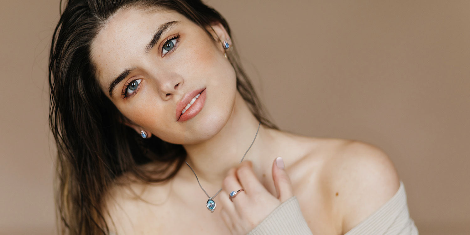 Junge Frau mit blauen Augen trägt blaue Ohrstecker, silberne Halskette mit blauem Anhänger und silbernen Ring